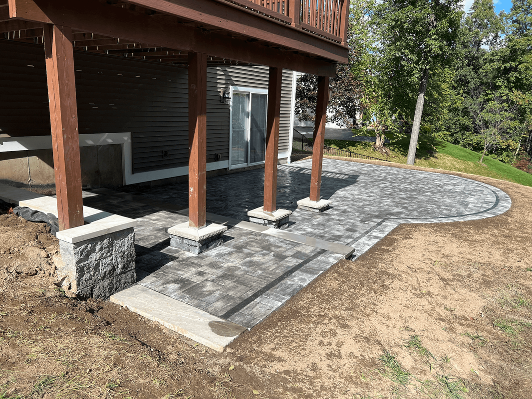 Gray pavers patio with rounded edge under a second story deck with concrete pillars surround the post